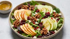 A vibrant green salad topped with red apple slices, cranberries, and candied walnuts in a large serving bowl.