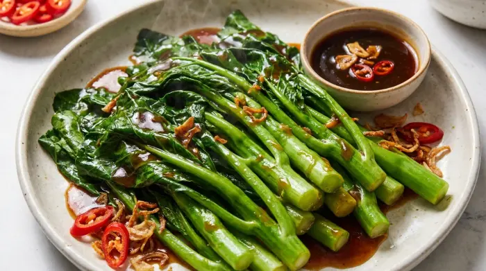 Steamed Chinese broccoli drizzled with garlic ginger oyster sauce on a serving plate.